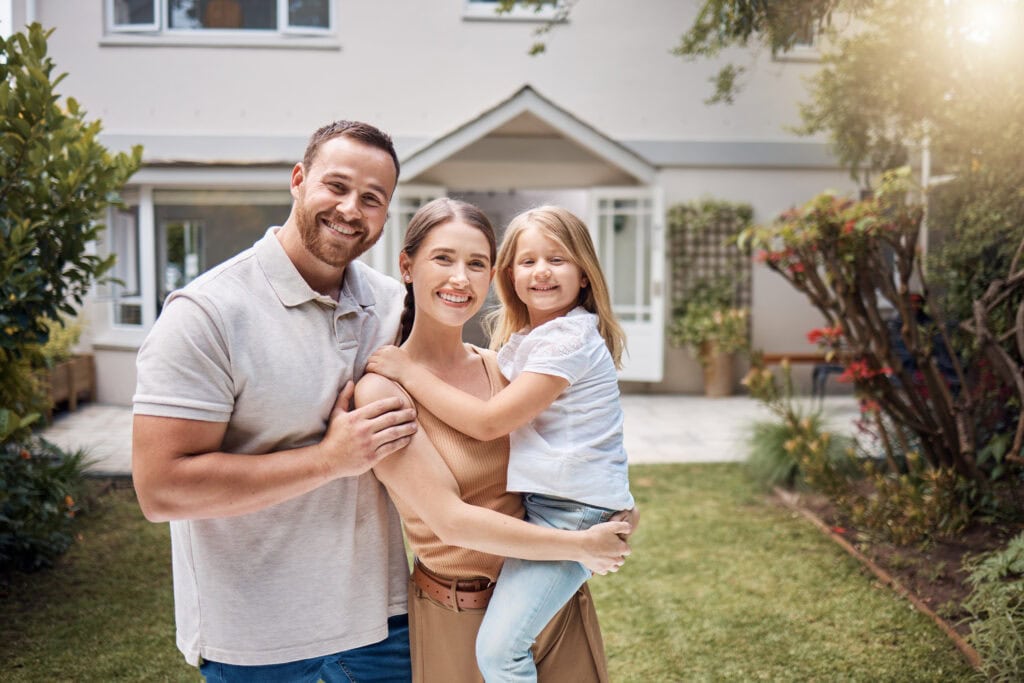 shot of a young couple standing outside and posing with their daughter in front of their house
